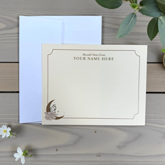Cream flat note card with gold moon and floral design, customizable name text at top, accompanied by white envelope.