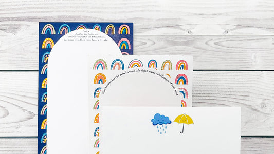 Set of stationery items with rainbow and cloud designs on a wooden surface