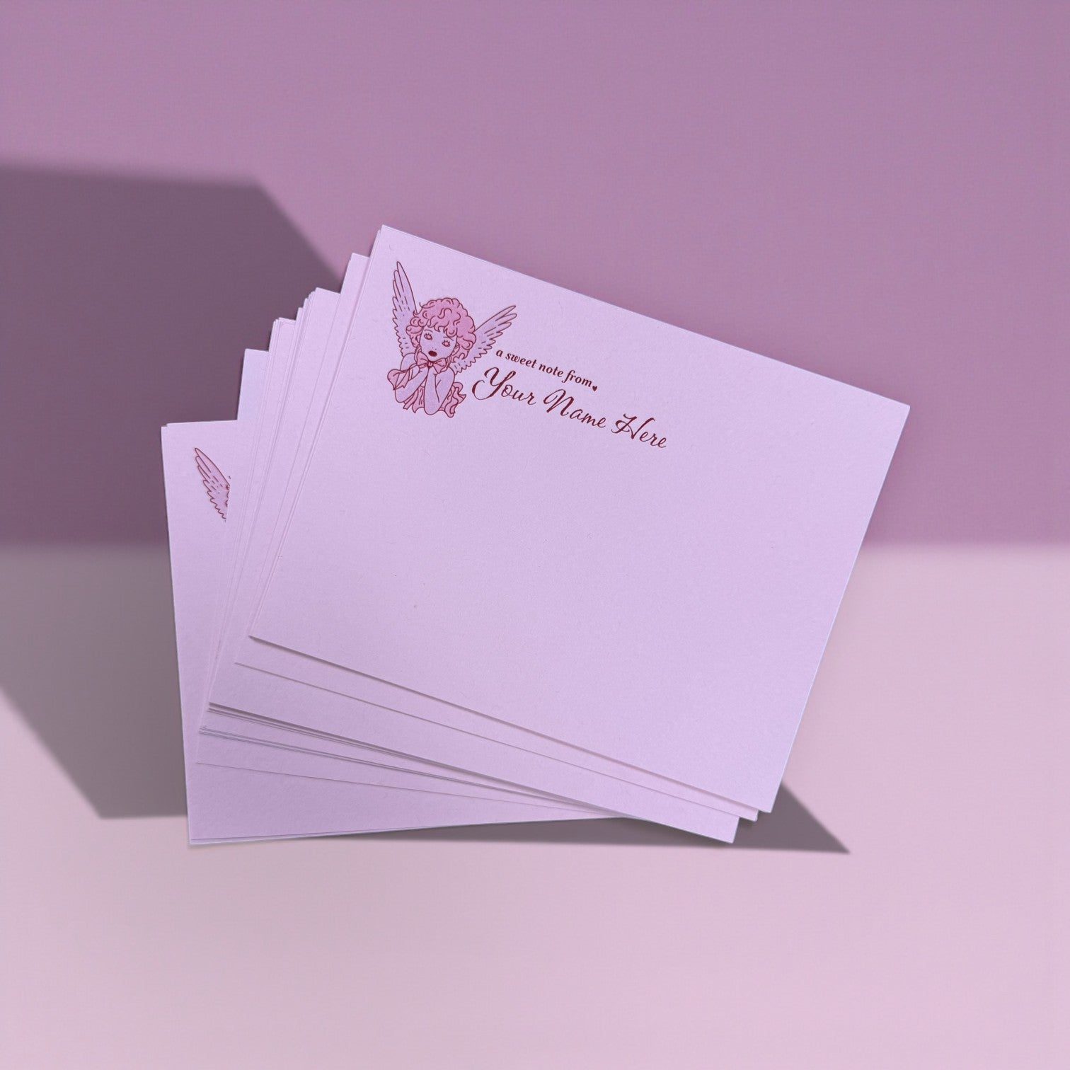 Set of pink notecards with a small angel illustration and personalized text in corner.