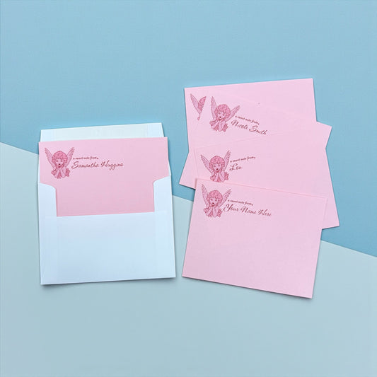Set of pink personalized notecards with angel graphic and cursive text, paired with white envelopes.