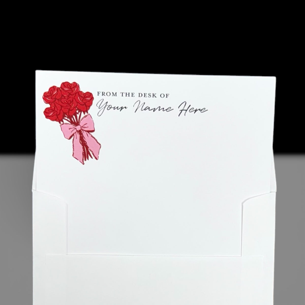 White notecard with red rose bouquet illustration tied with a pink ribbon and customizable "From the Desk of Your Name Here" .