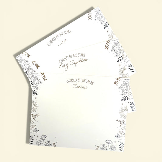 Set of three white flat note cards with black and gold celestial floral border and personalized text in script and uppercase .