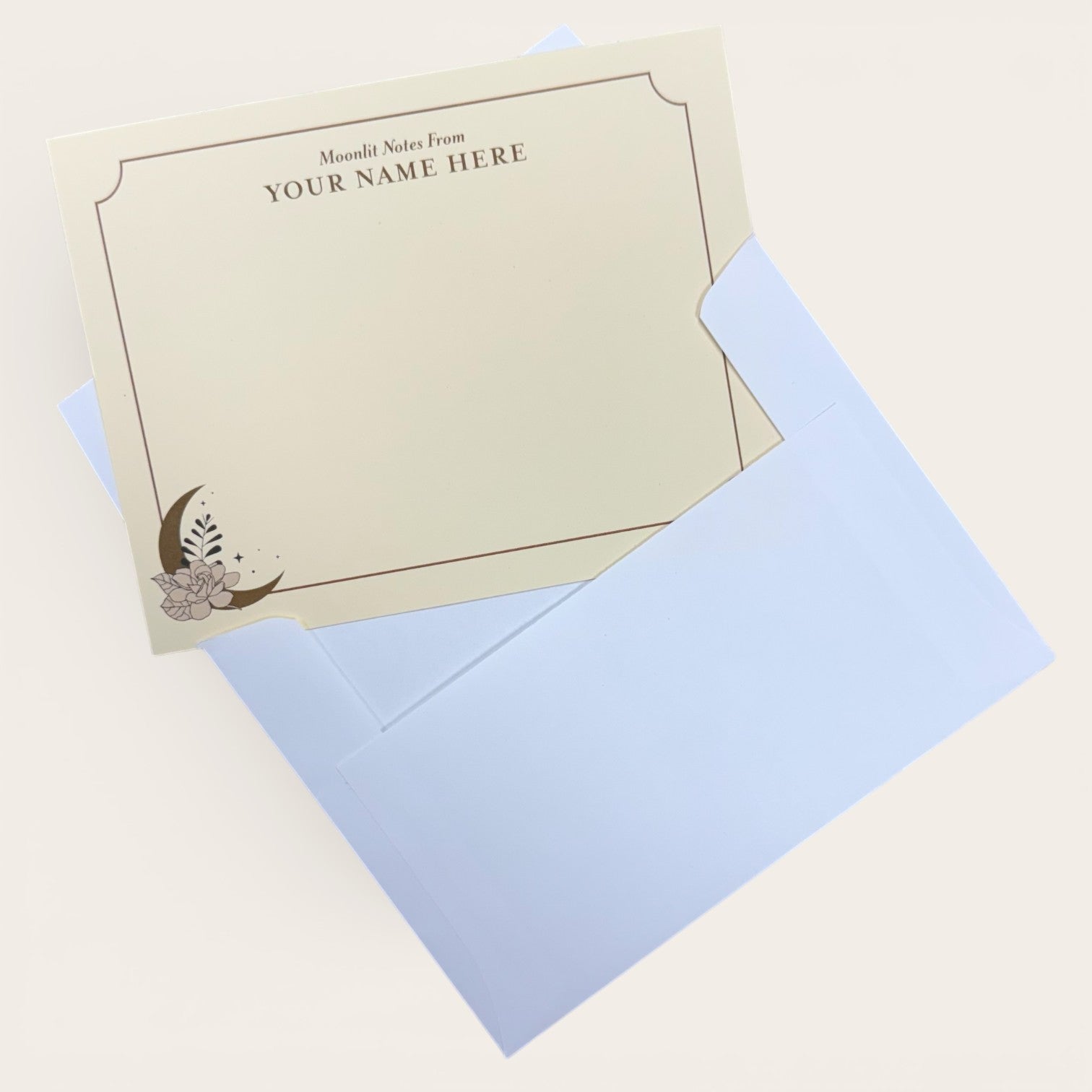 Flat cream note card with customizable name text, delicate floral and crescent moon design, paired with light blue envelope.