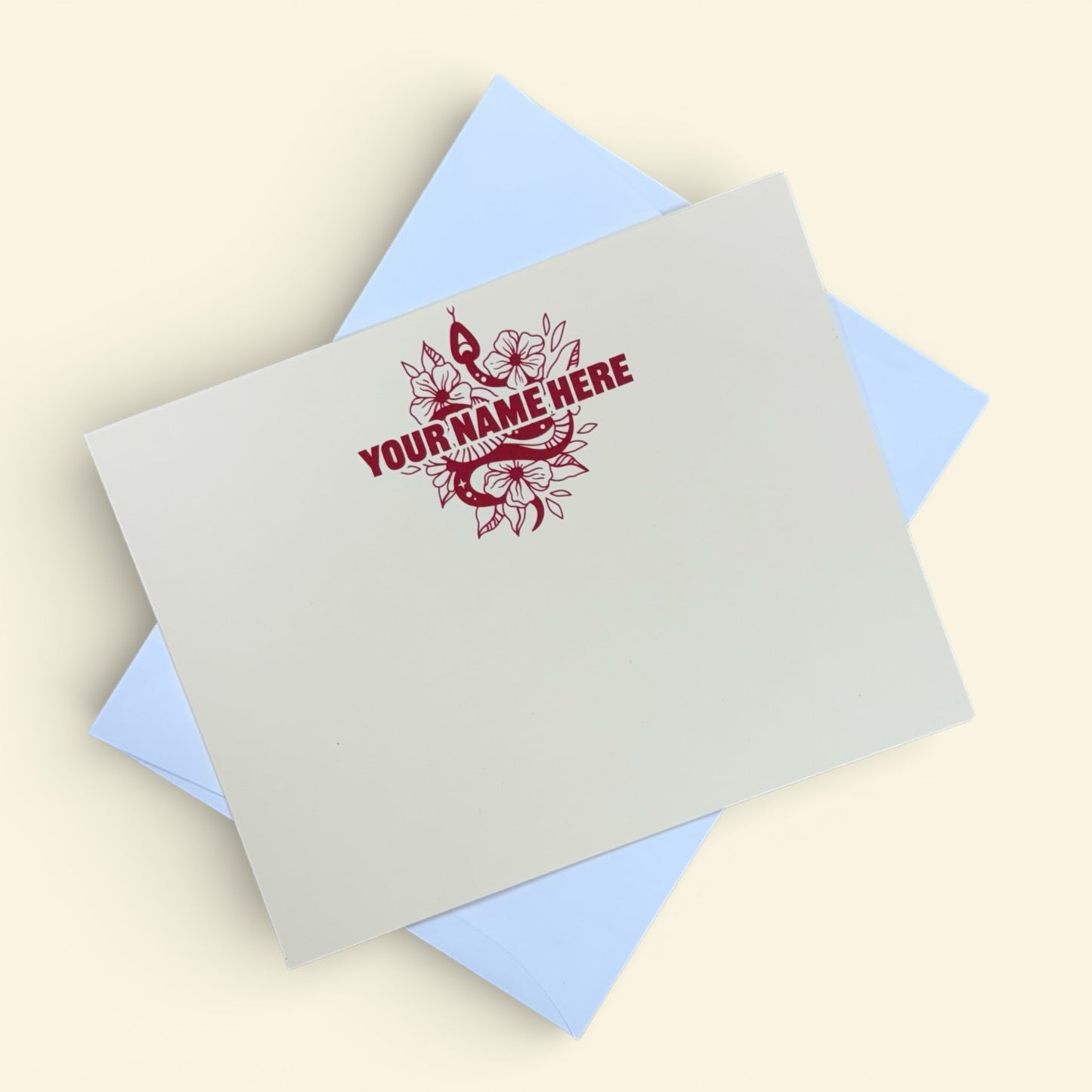 Cream-colored notecard with personalized maroon snake and floral design above customizable text, paired with a light blue.