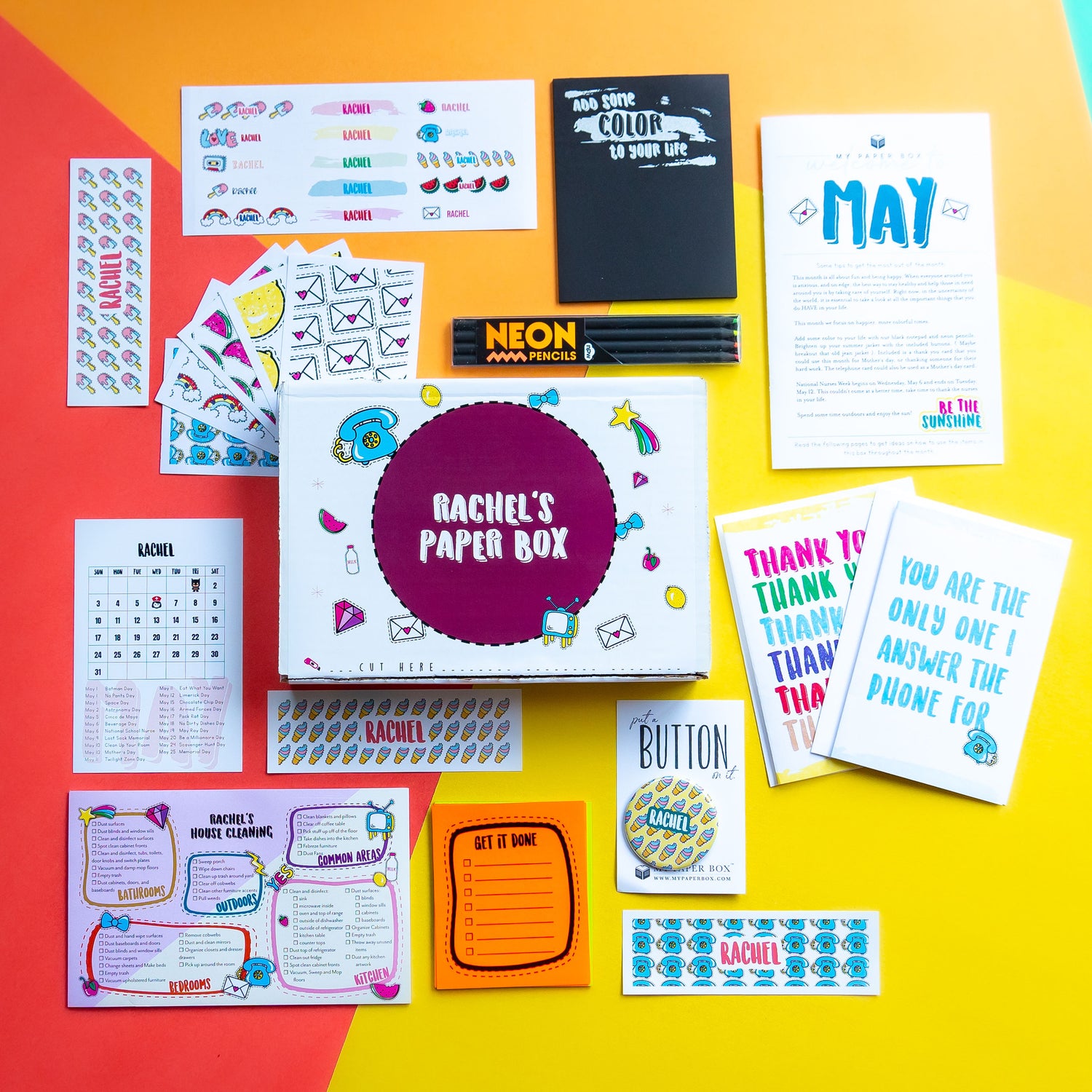 Collection of stationery items including cards, stickers, and a box labeled 'Rachel's Paper Box' on a colorful background.