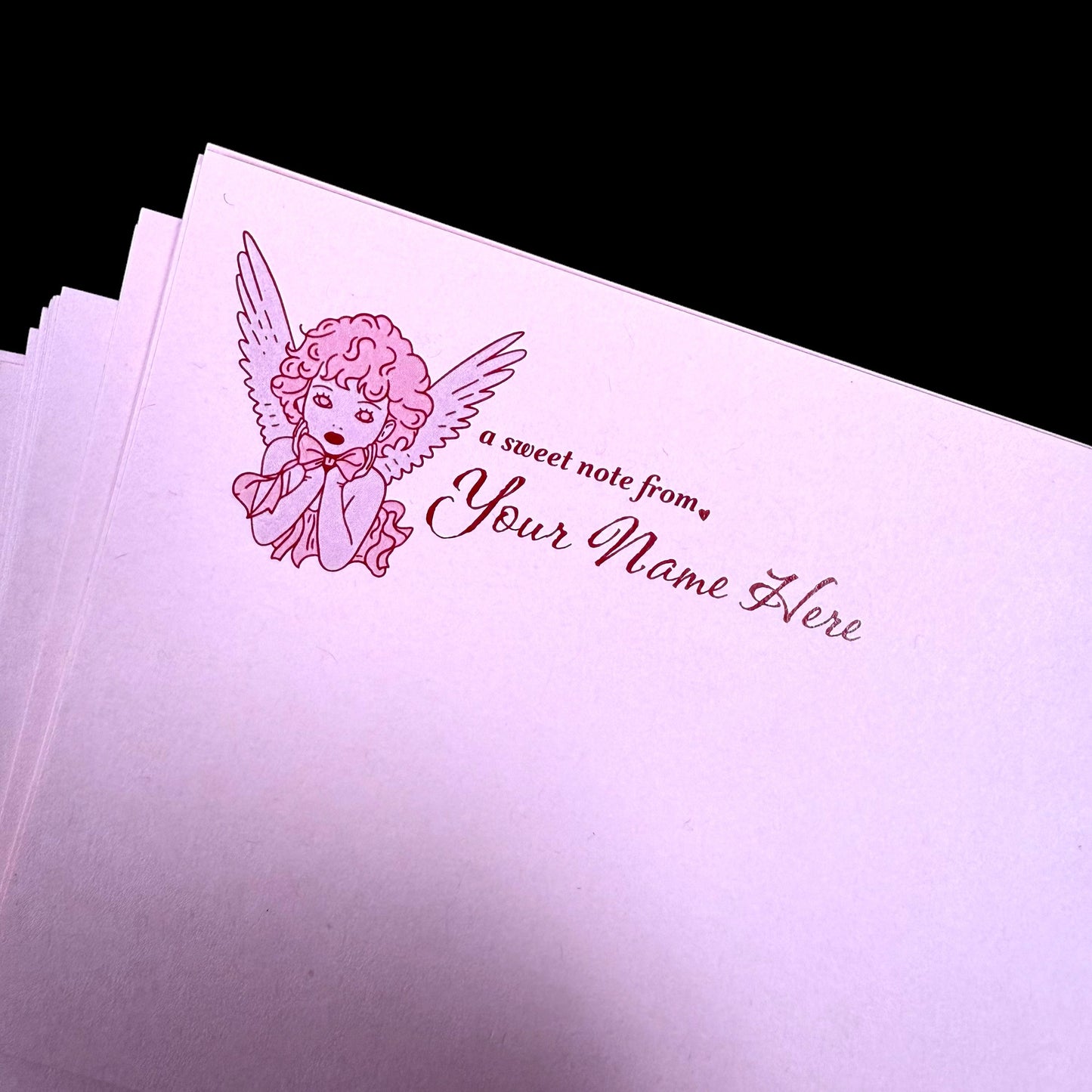 Pink stationery with angel illustration and customizable text on a black background