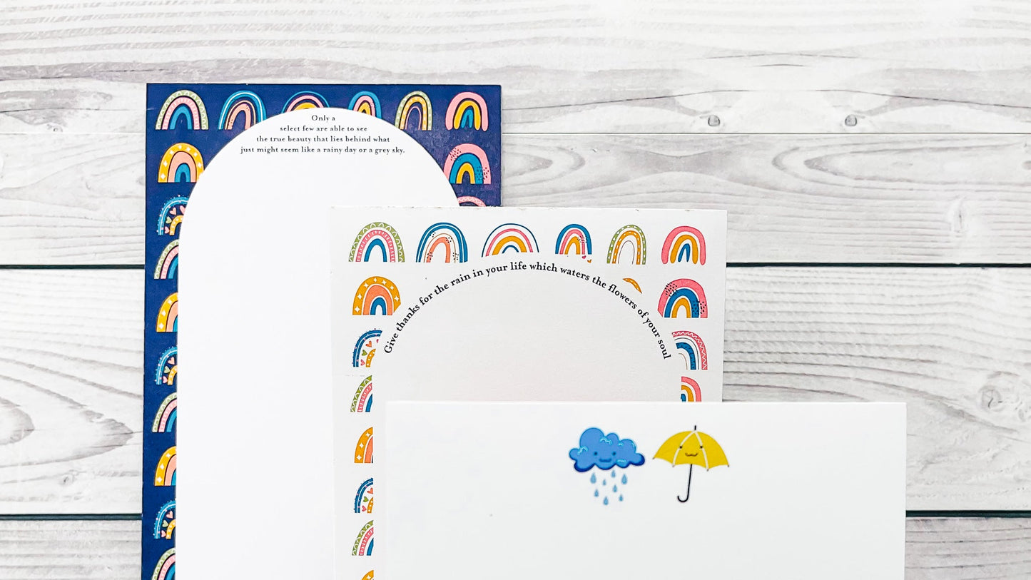 Set of stationery items with rainbow and cloud designs on a wooden surface